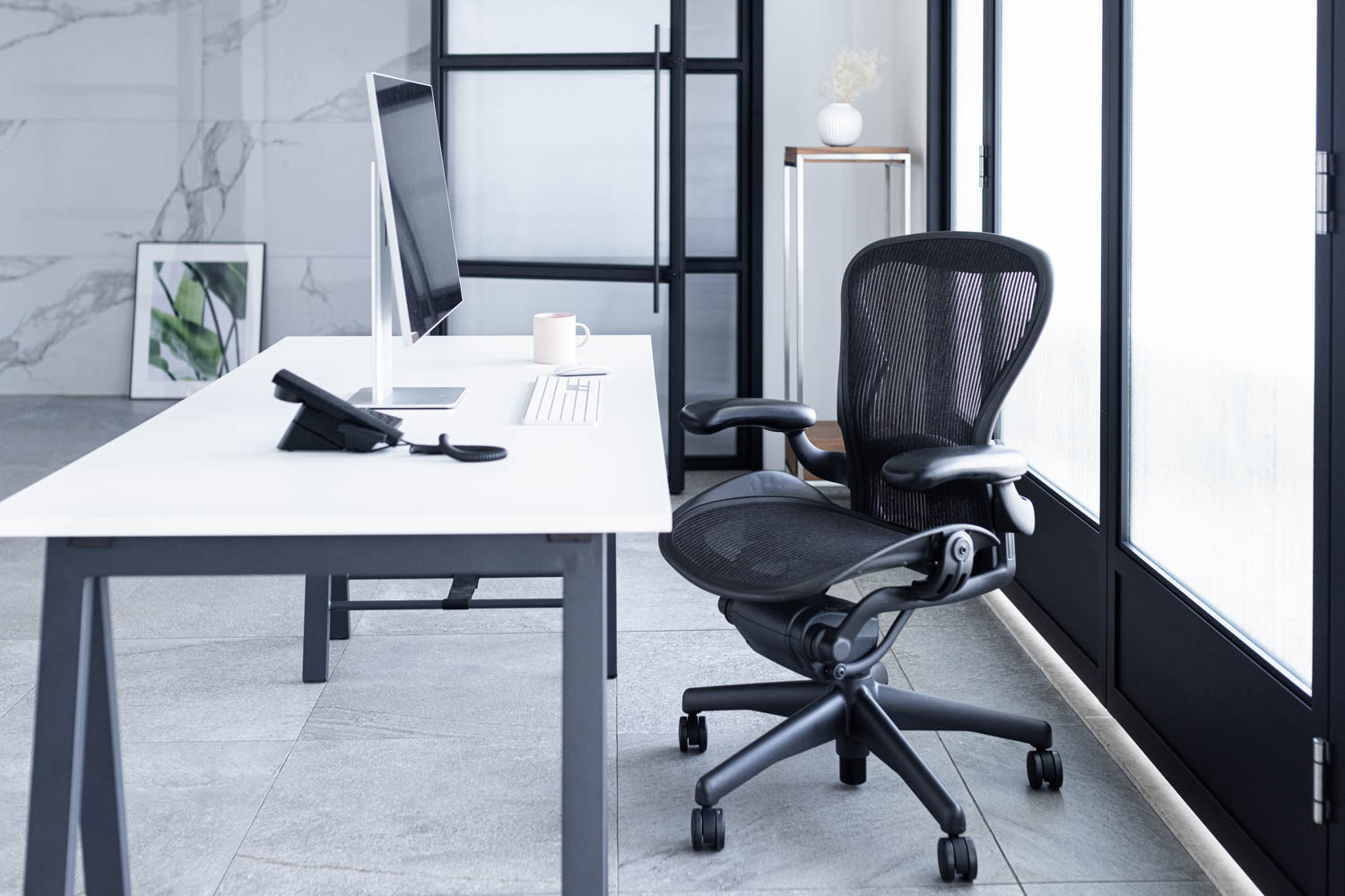 モノトーンの空間に、白いデスクが置かれたオフィス風の写真