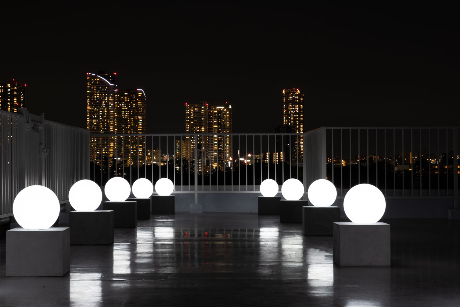 夜間の屋上で、夜景を背景に並んだライティングボールが白く光る写真