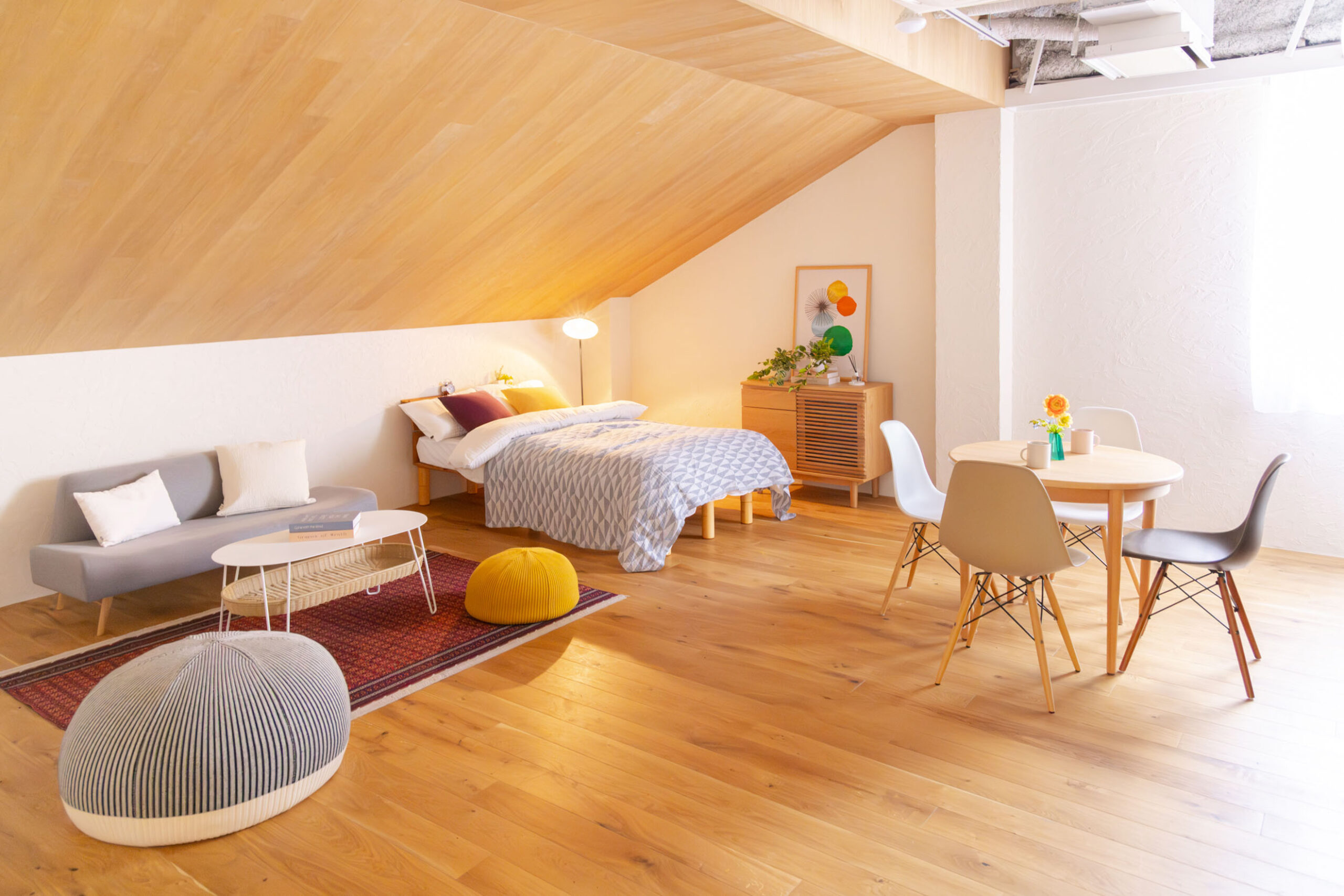 斜め天井でナチュラルウッド調の部屋に、ベットなど北欧家具が置かれた写真