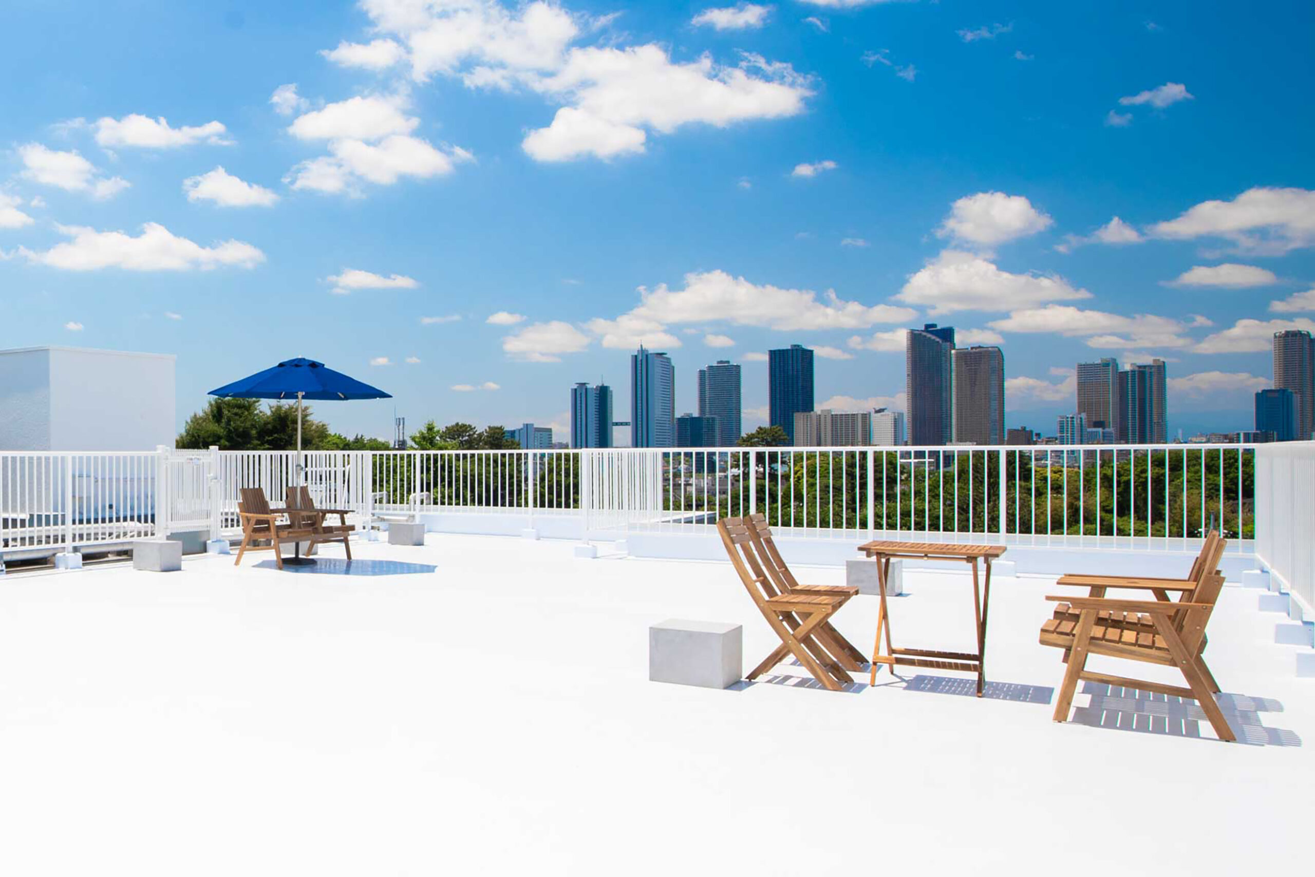 青空の屋上の写真。手前にはパラソルと木製の家具があり、奥にはビル群が見える写真